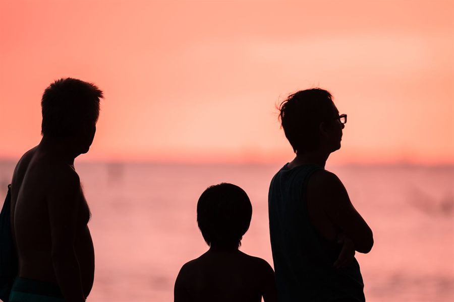 Silhouettes of a family of three watching the sunset on a Hawaiian beach