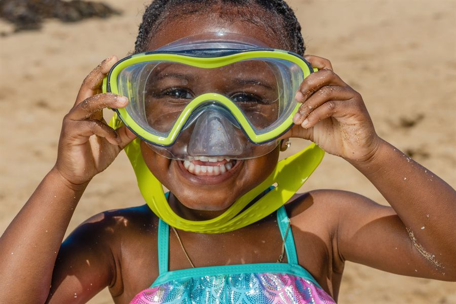 Smiling girl holding up a snorkel mask on the beach