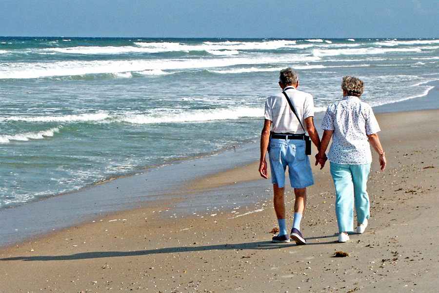 Older couple walking hand in hand along the edge of the surf on a sandy beach