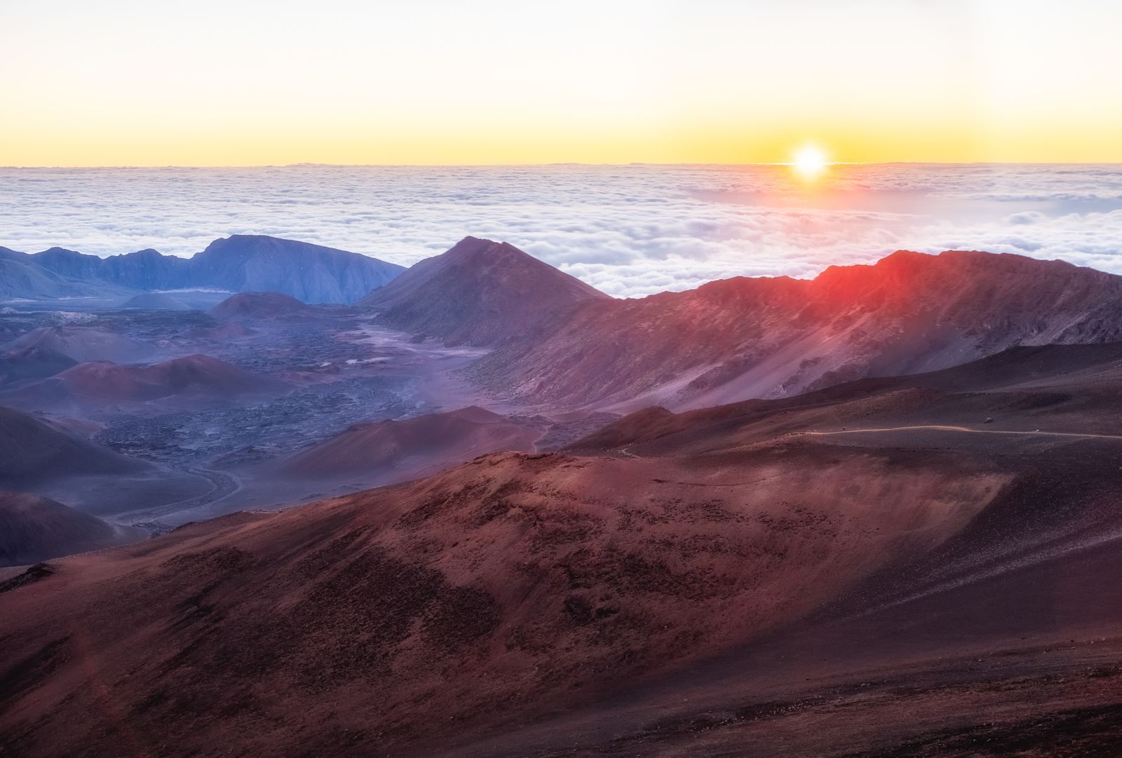 Sunrise over the Haleakalā crater on Maui, with cinder cones below and clouds on the horizon